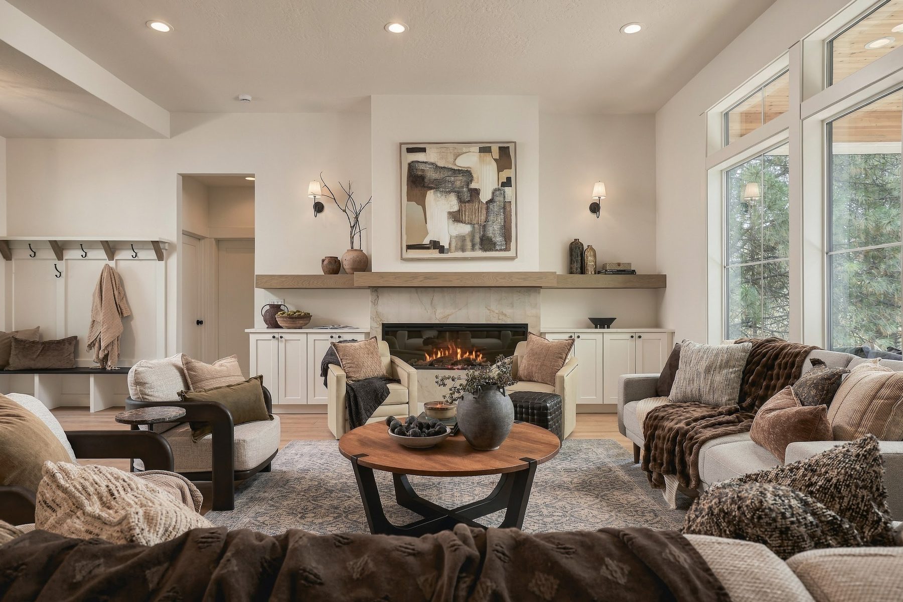 Great room with a stone fireplace, timber mantel and tall windows onto the trees